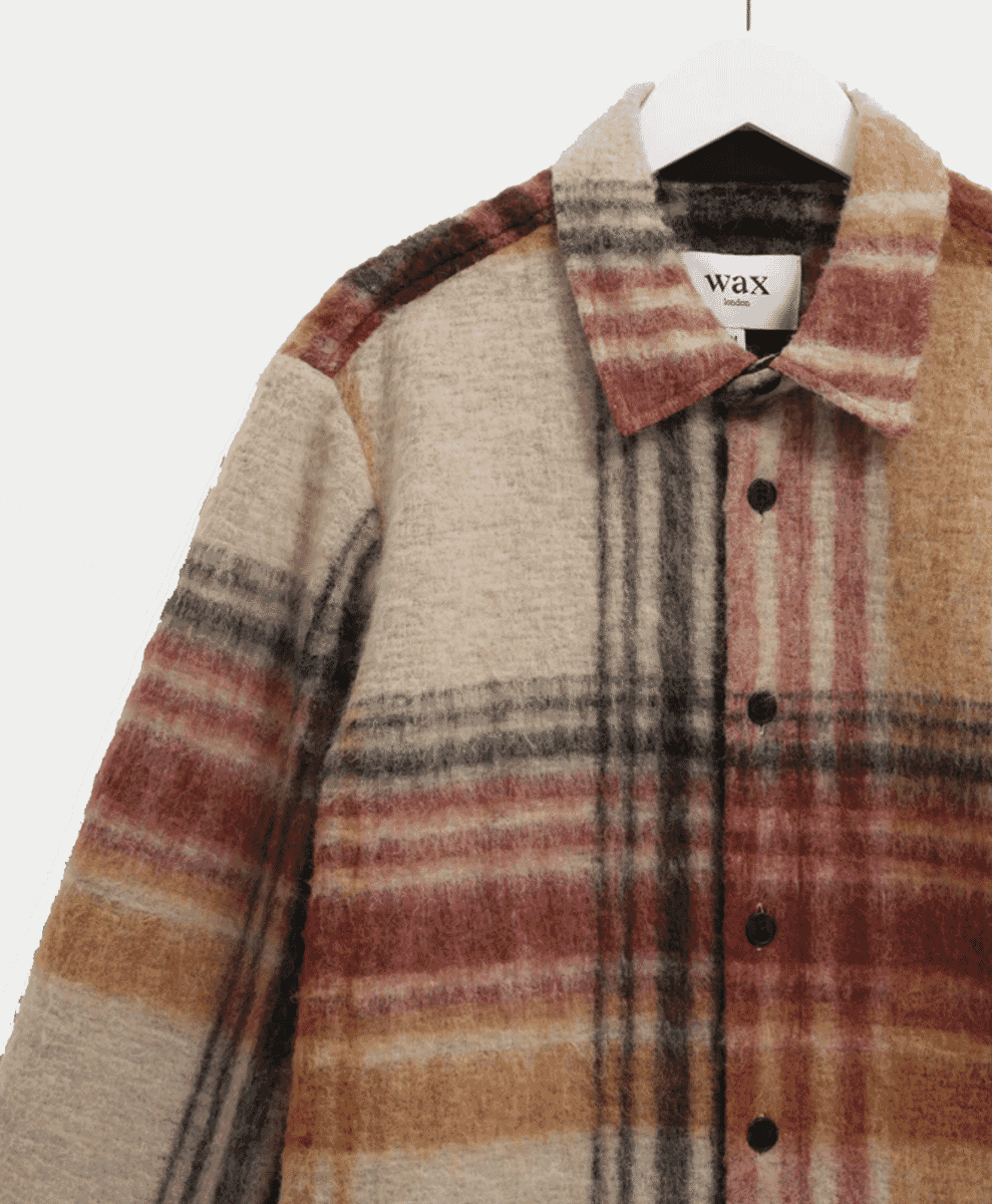 Close-up of a multi-color plaid wool overshirt by Wax London on a hanger.