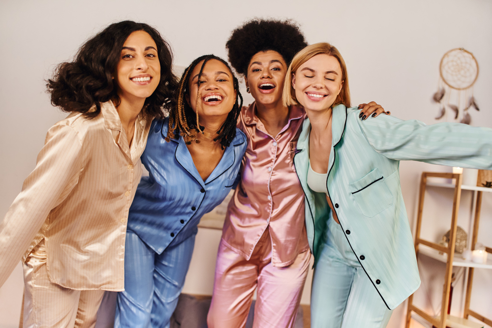 Four diverse women posing indoors in colorful satin pajamas in shades of beige, blue, pink, and mint green.