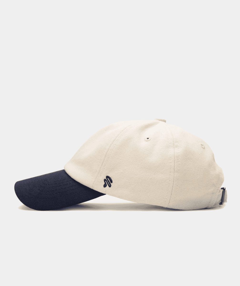 Side profile of a two-tone baseball cap with an off-white crown and navy blue brim.