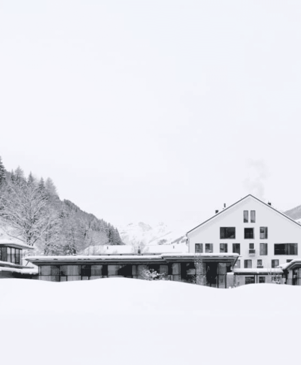 Atmospheric black-and-white landscape of snow-covered mountains and alpine architecture.