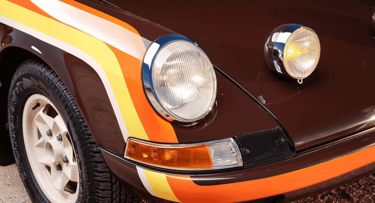Close-up of a classic brown Porsche with orange and yellow racing stripes and round headlights.