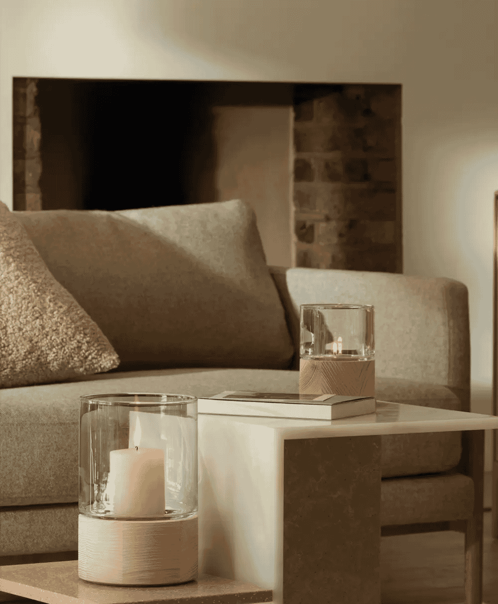 A cozy living room featuring glass candle holders on a marble side table near a neutral sofa.