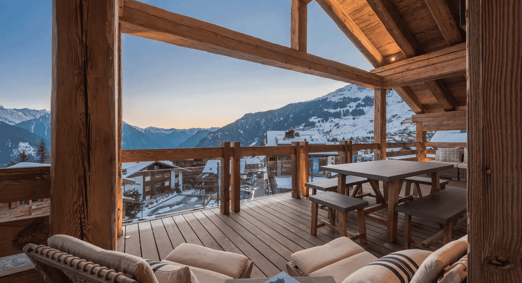 Twilight shot of a mountain lodge balcony with rustic seating overlooking a snowy valley.