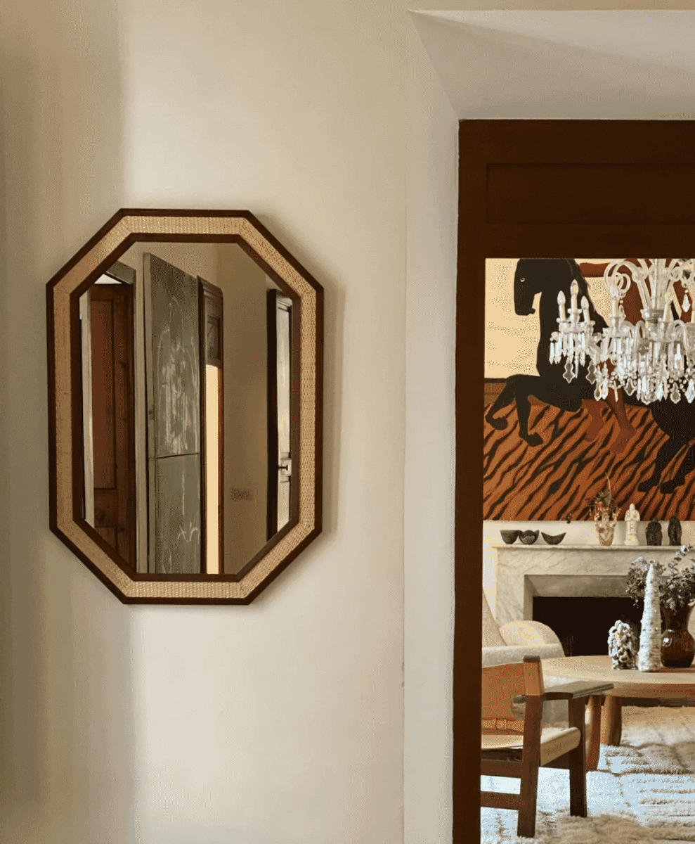 An octagonal rattan-framed mirror hanging in a curated modern interior.
