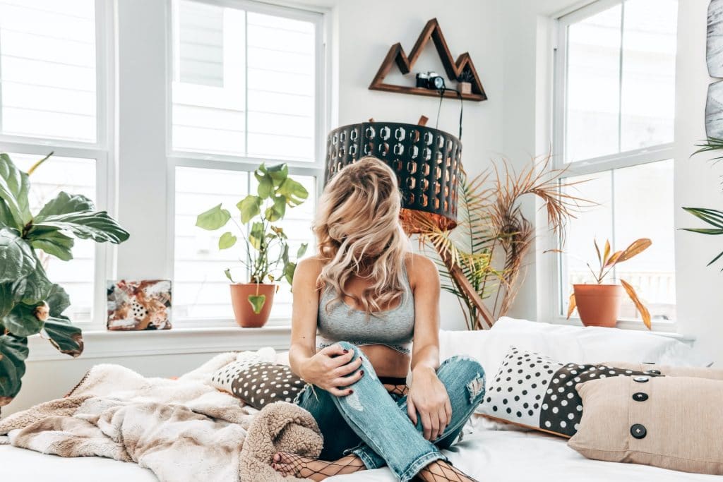 Woman in a boho-chic bedroom setting wearing ripped jeans and fishnet stockings.
