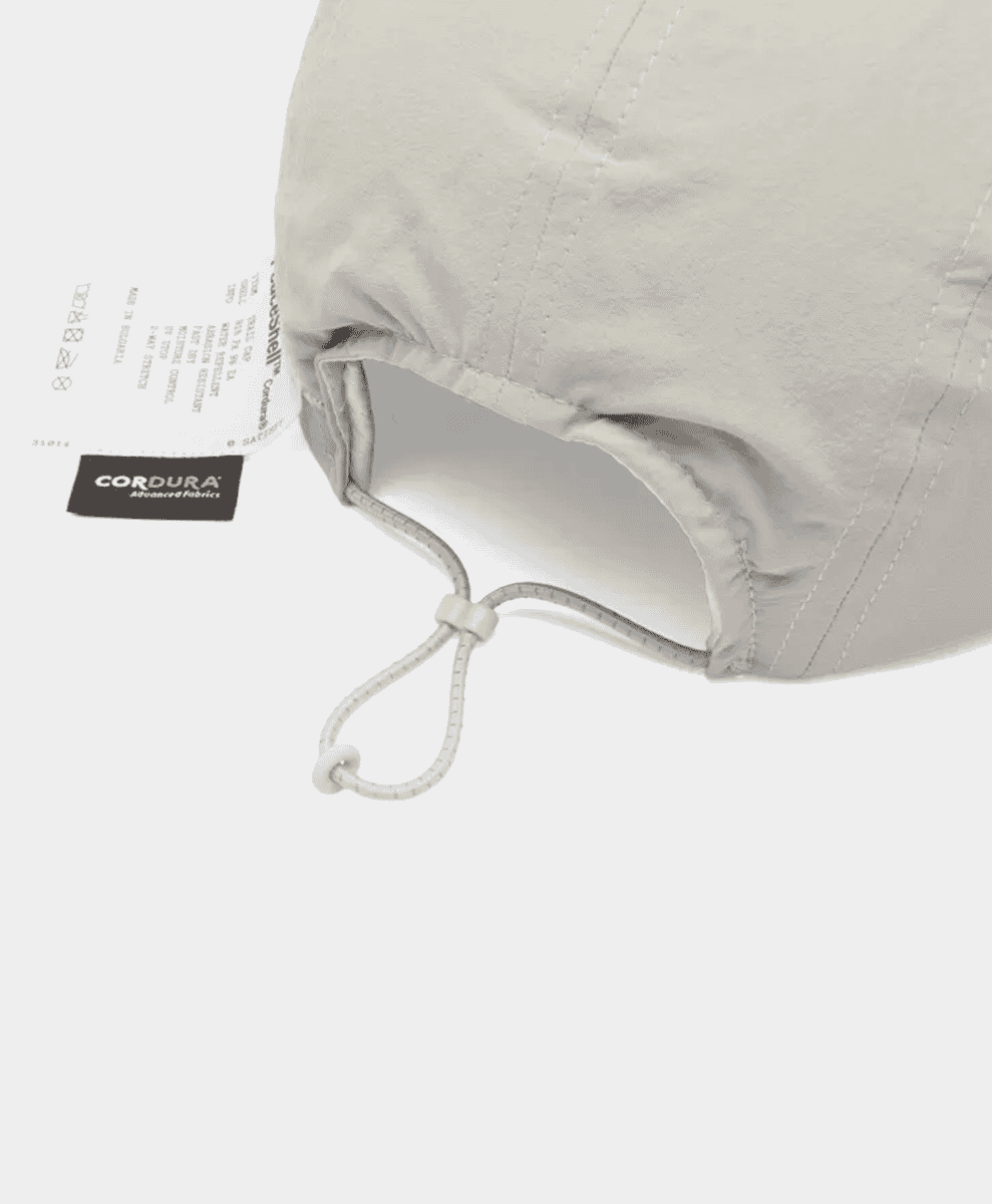 Close-up of a gray outdoor cap featuring a Cordura fabric tag and adjustable drawstring.