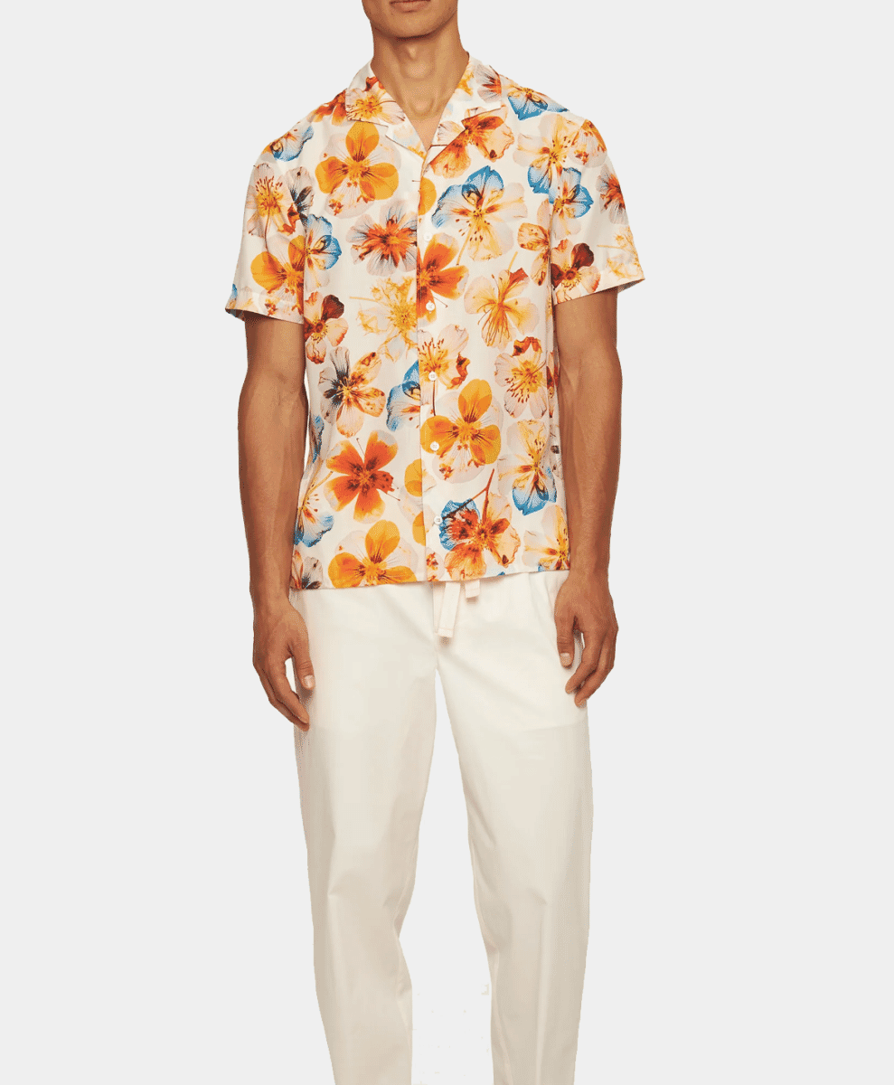 Man in a vibrant orange and blue floral print shirt with white trousers.
