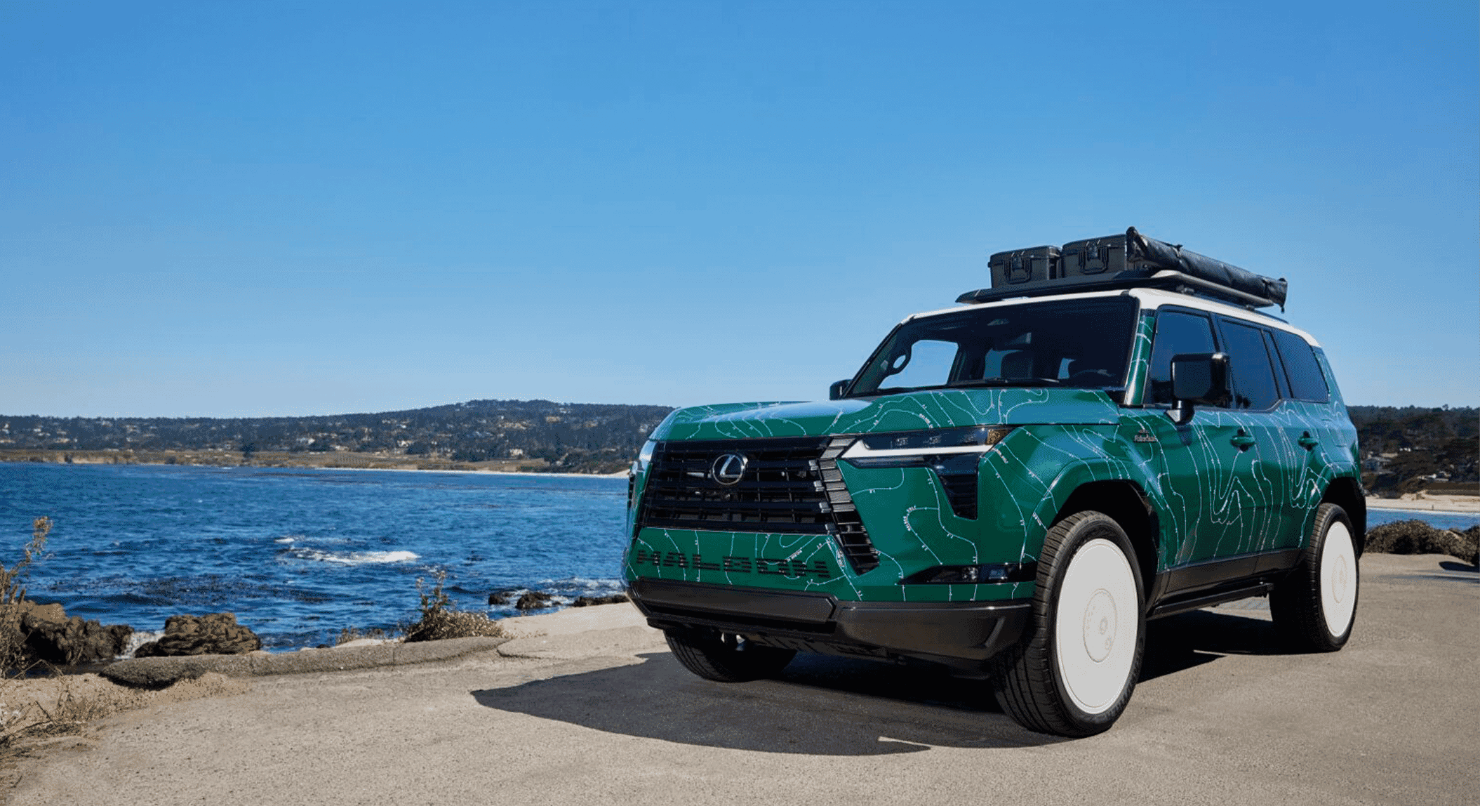 Wide shot of the green Lexus SUV with white topographic lines on a coastal road.