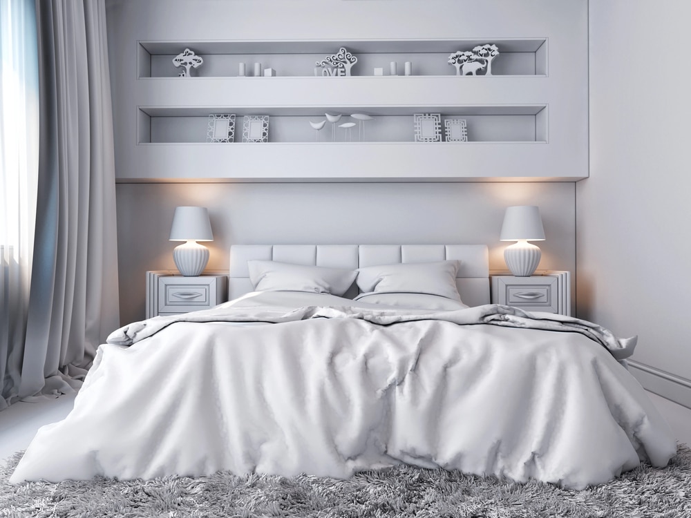 Minimalist white bedroom with plush bedding and built-in shelves containing decorative objects.