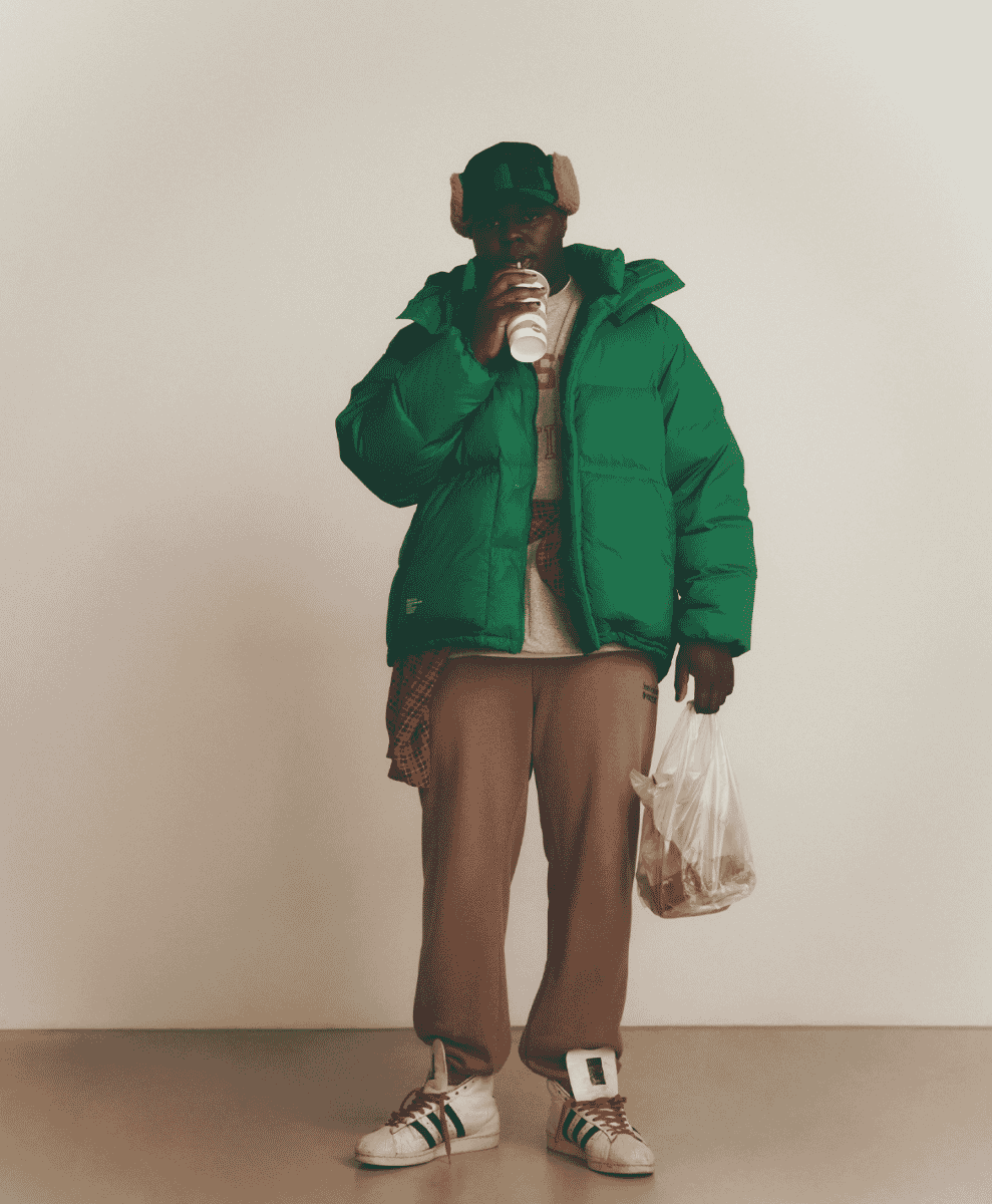 Man in a vibrant green puffer jacket holding a cup and plastic bag in a casual pose.