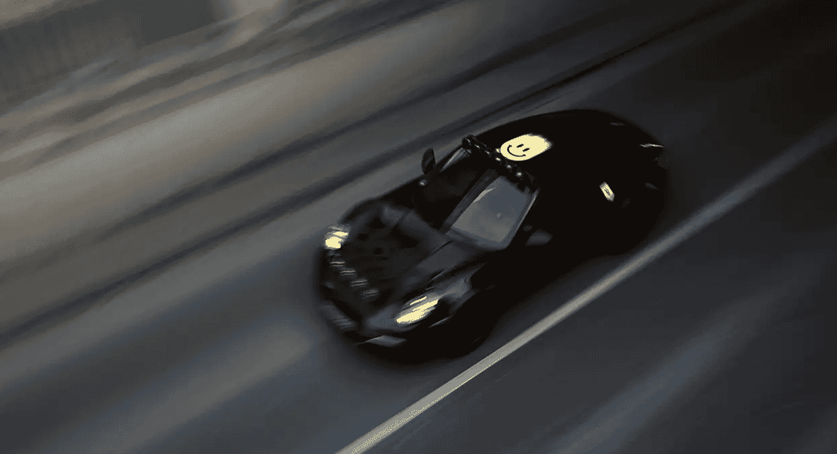 A black Porsche 911 with a yellow smiley face sticker on its roof speeding on a blurred highway at night.