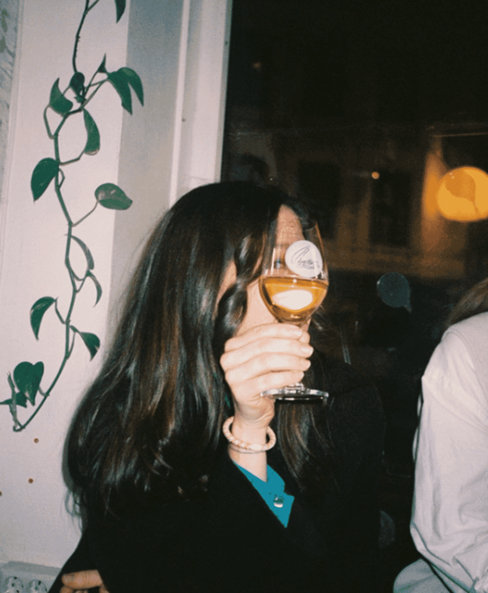 A woman in a black coat and teal shirt holding a wine glass.