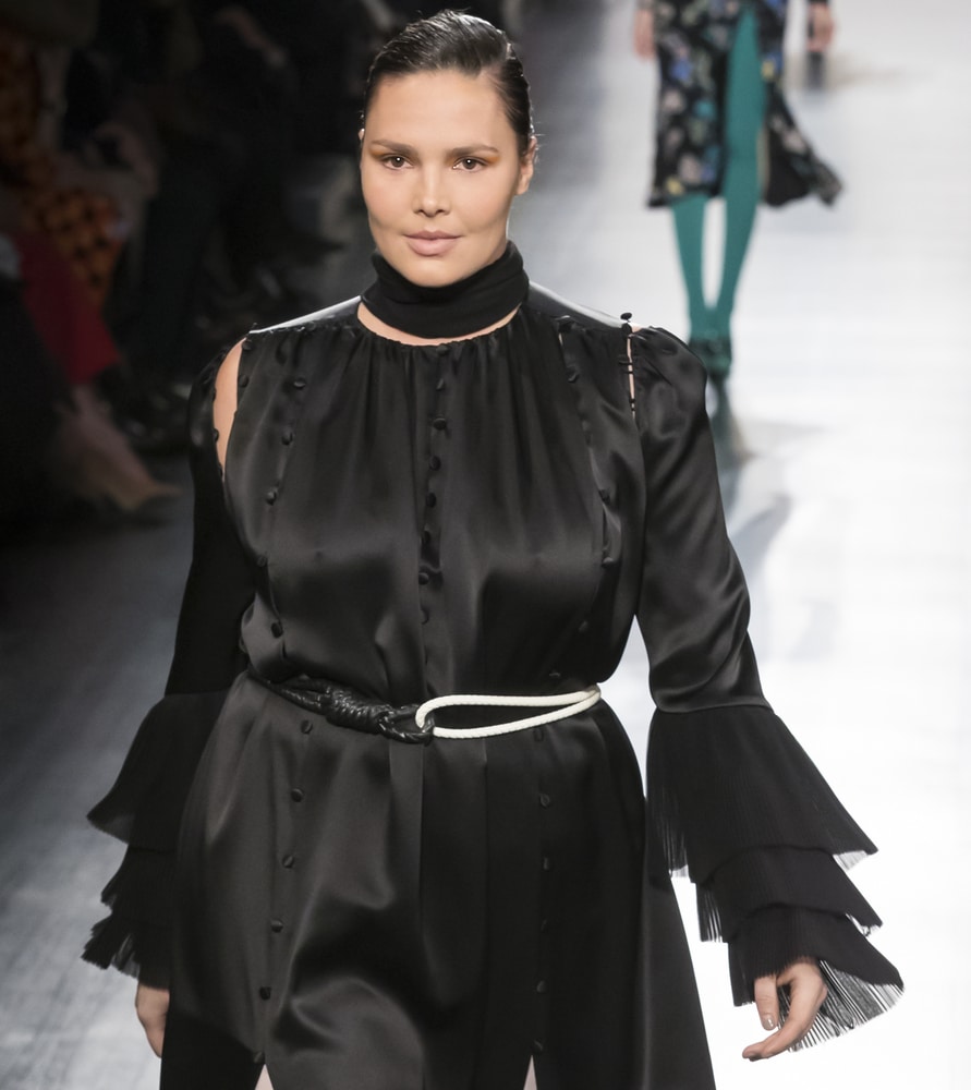 A model in a dramatic black satin dress with ruffled bell sleeves and a high neck collar.