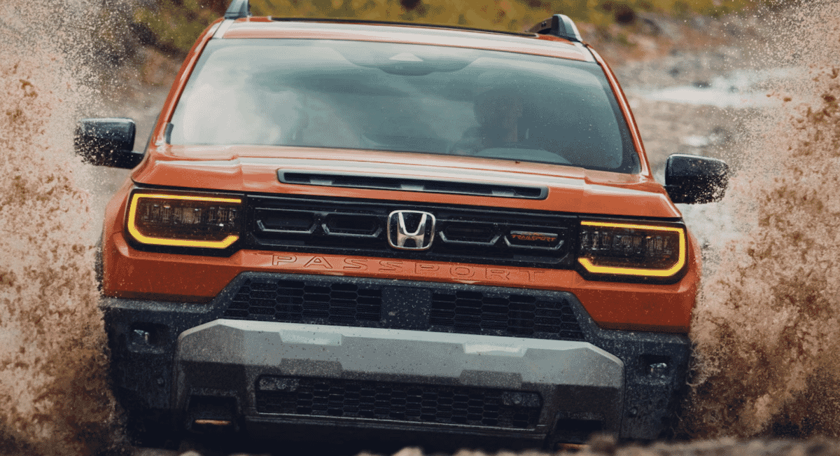An orange Honda Passport TrailSport SUV splashing through muddy water.