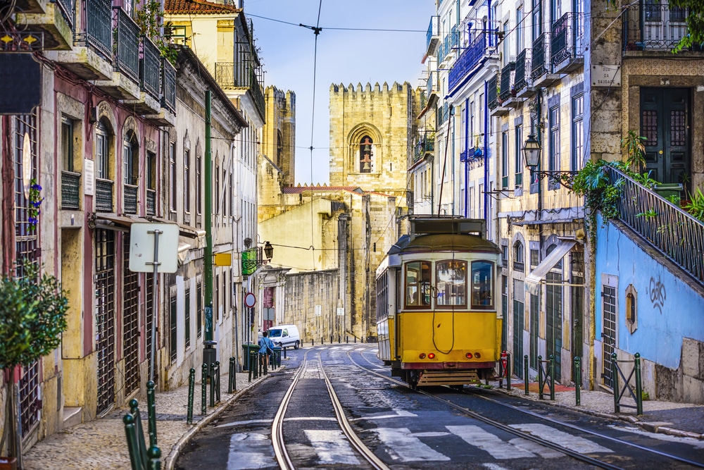 A yellow vintage tram on a narrow street in Lisbon surrounded by colorful, historic buildings.