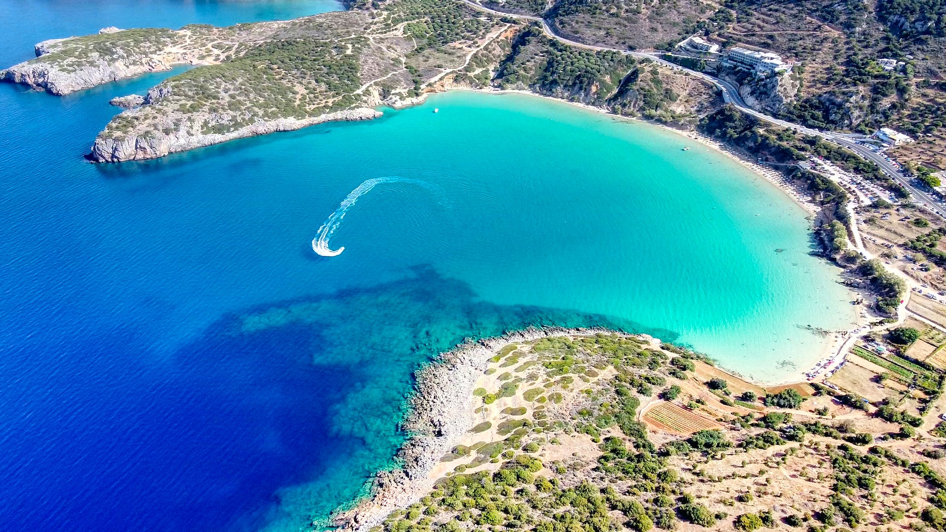 Aerial drone view of a speedboat cruising through turquoise coastal waters surrounded by tropical cliffs.