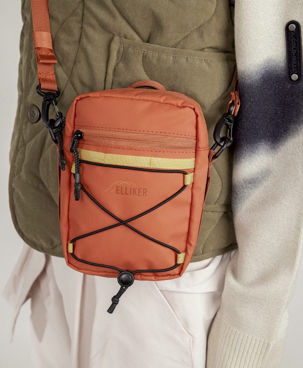 A person wearing a vibrant orange Elliker crossbody bag over an olive quilted vest.