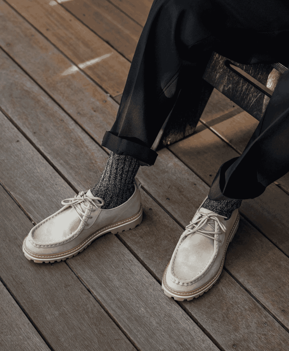 Close-up of a man wearing white chunky-sole loafers and navy ribbed socks on a wooden deck.