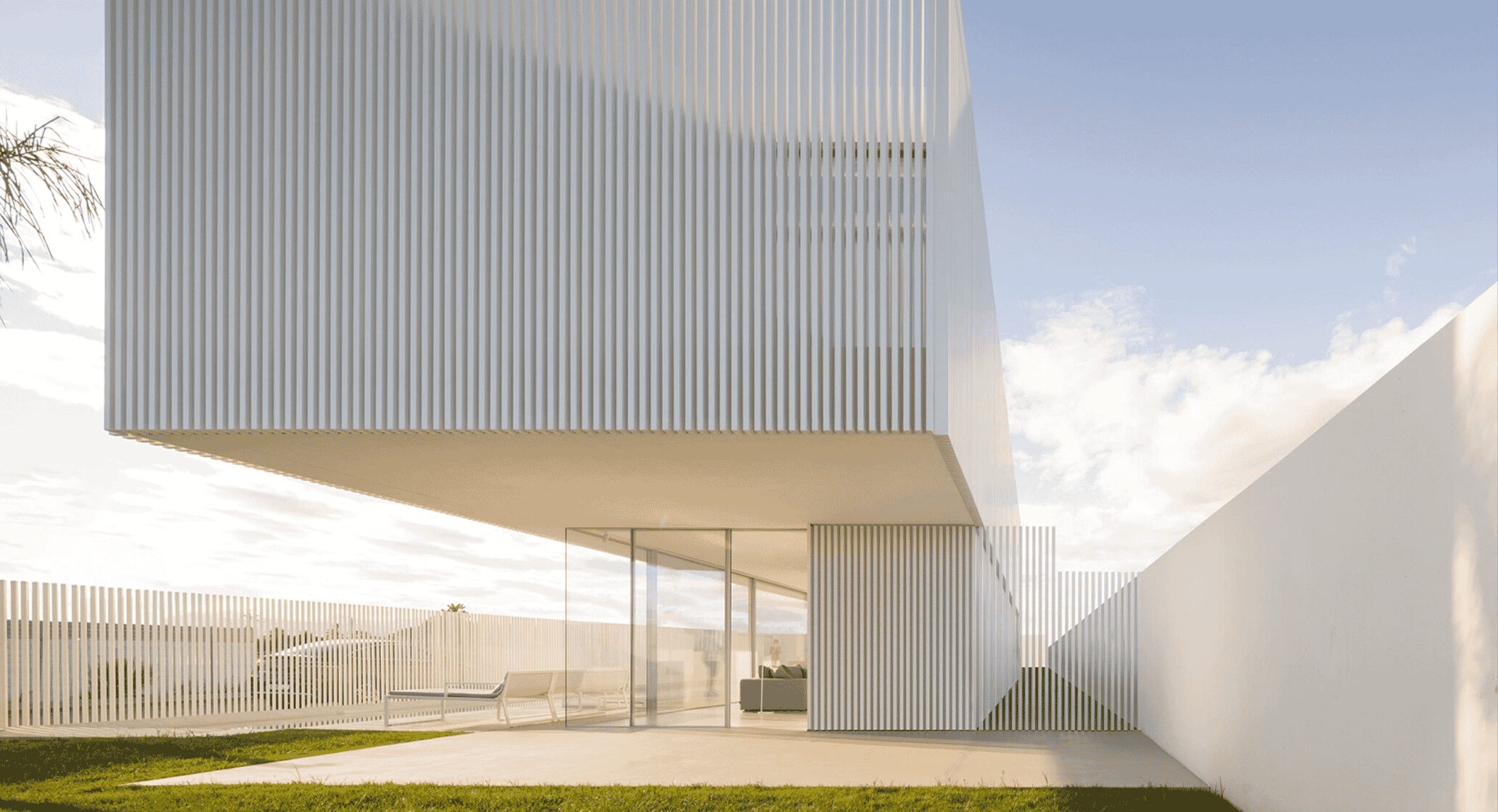 Modern white architectural facade with vertical slats and glass walls under a bright sky.