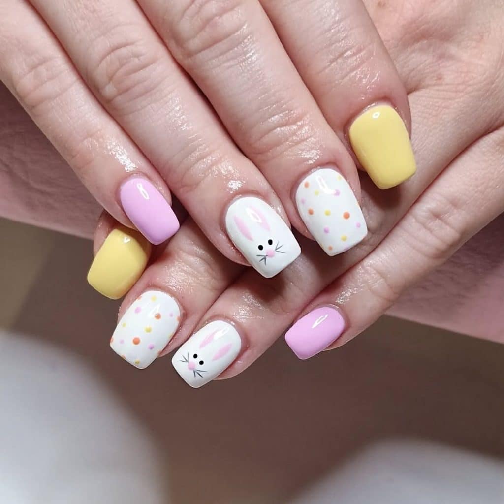 Nail art featuring bunny faces and pastel polka dots on soft pink and yellow polish.