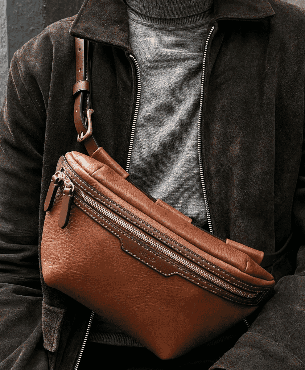 Man in a dark suede jacket and grey turtleneck wearing a brown leather crossbody bag.