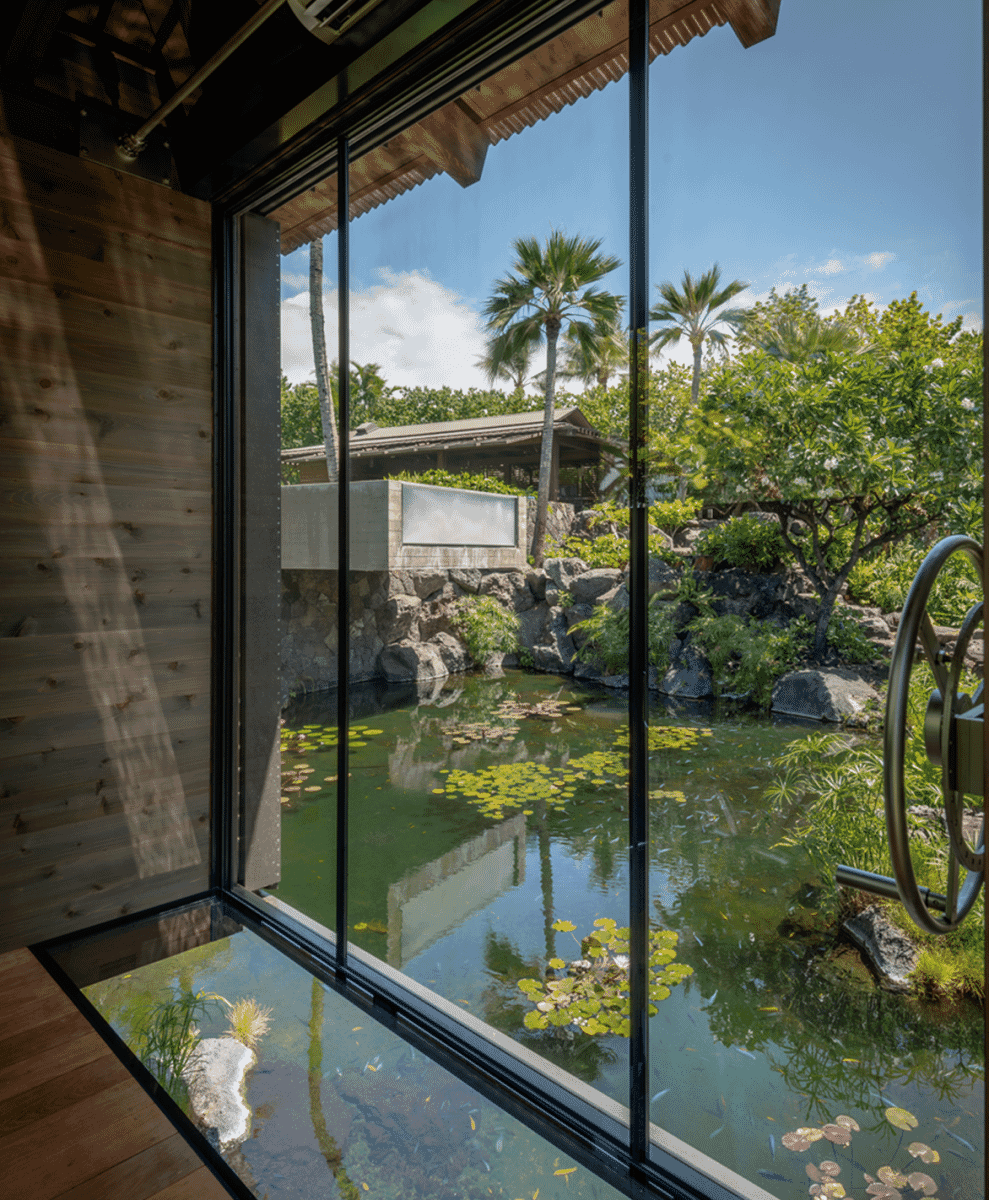 Interior view looking out through large windows toward a tranquil pond with lily pads.