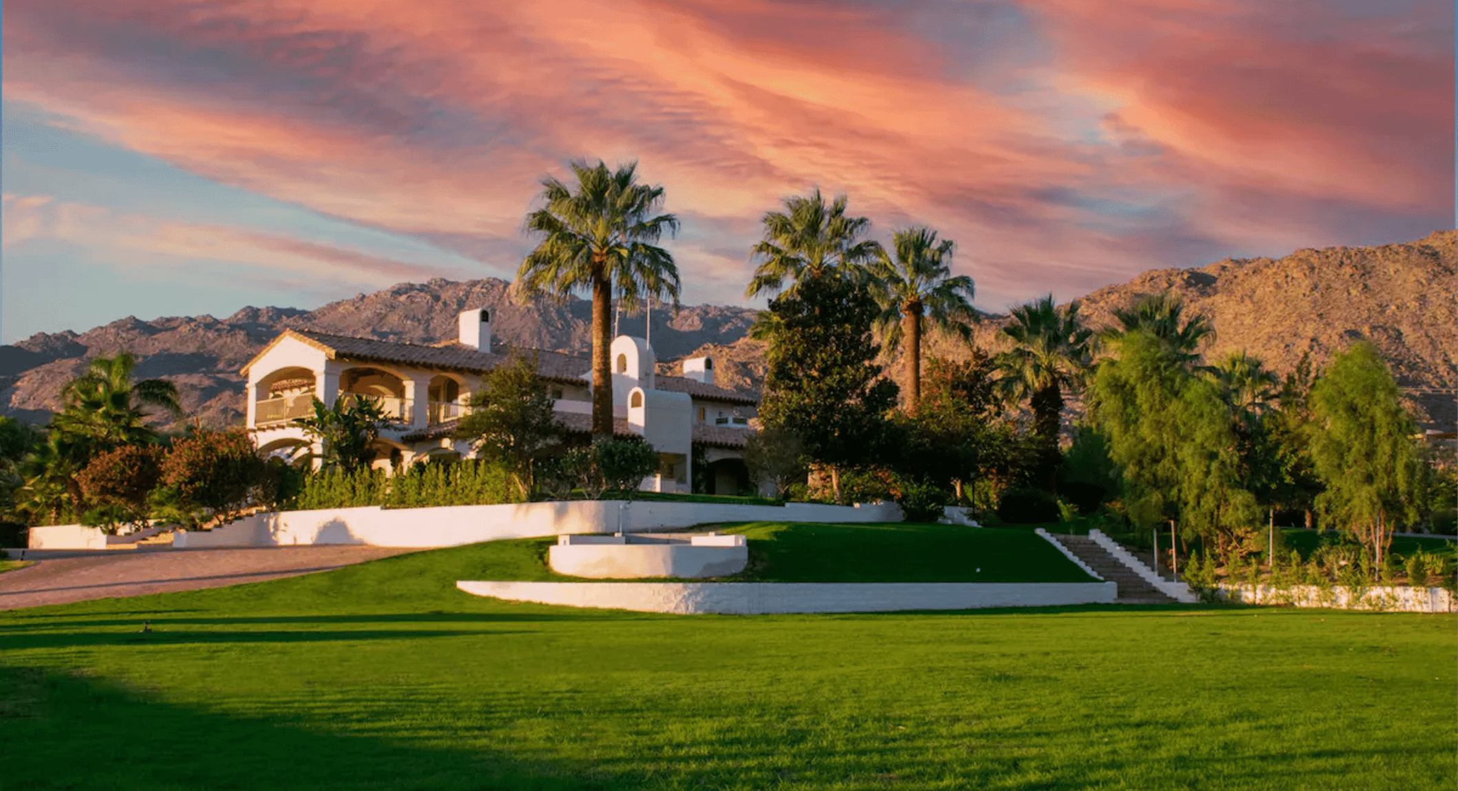 Mediterranean villa with white stucco walls glowing at sunset against a mountain backdrop.