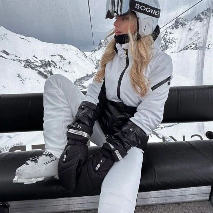 Woman in a white and black Bogner ski suit and helmet sitting on a chairlift.