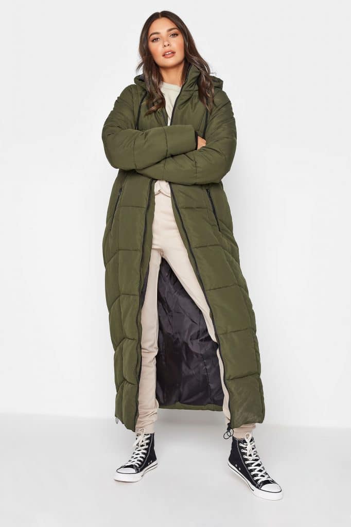 Woman modeling a long olive green quilted puffer coat with a hood.