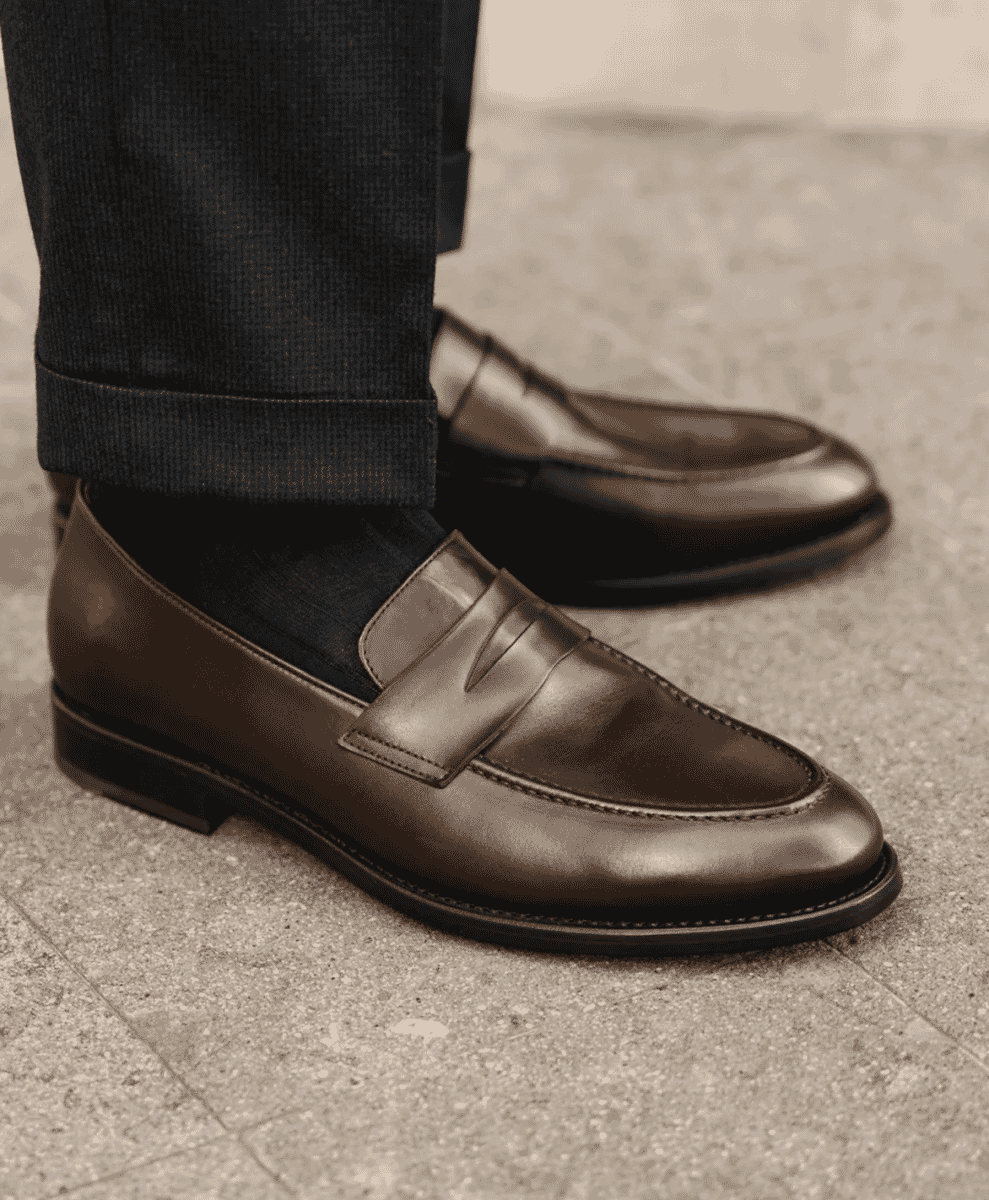 Close-up of a man wearing polished brown leather penny loafers with cuffed trousers.