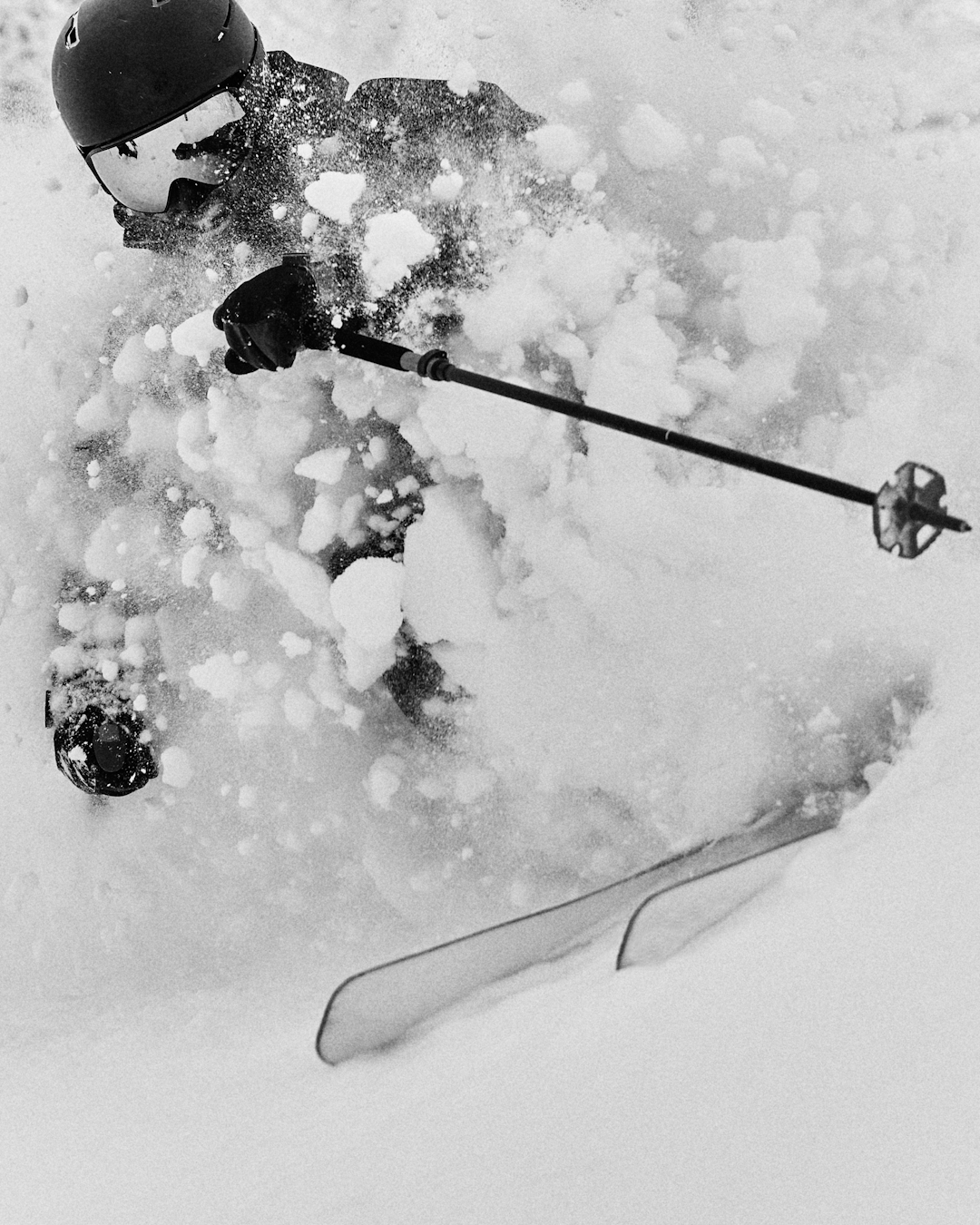 Black and white action shot of a skier carving through deep powder snow.