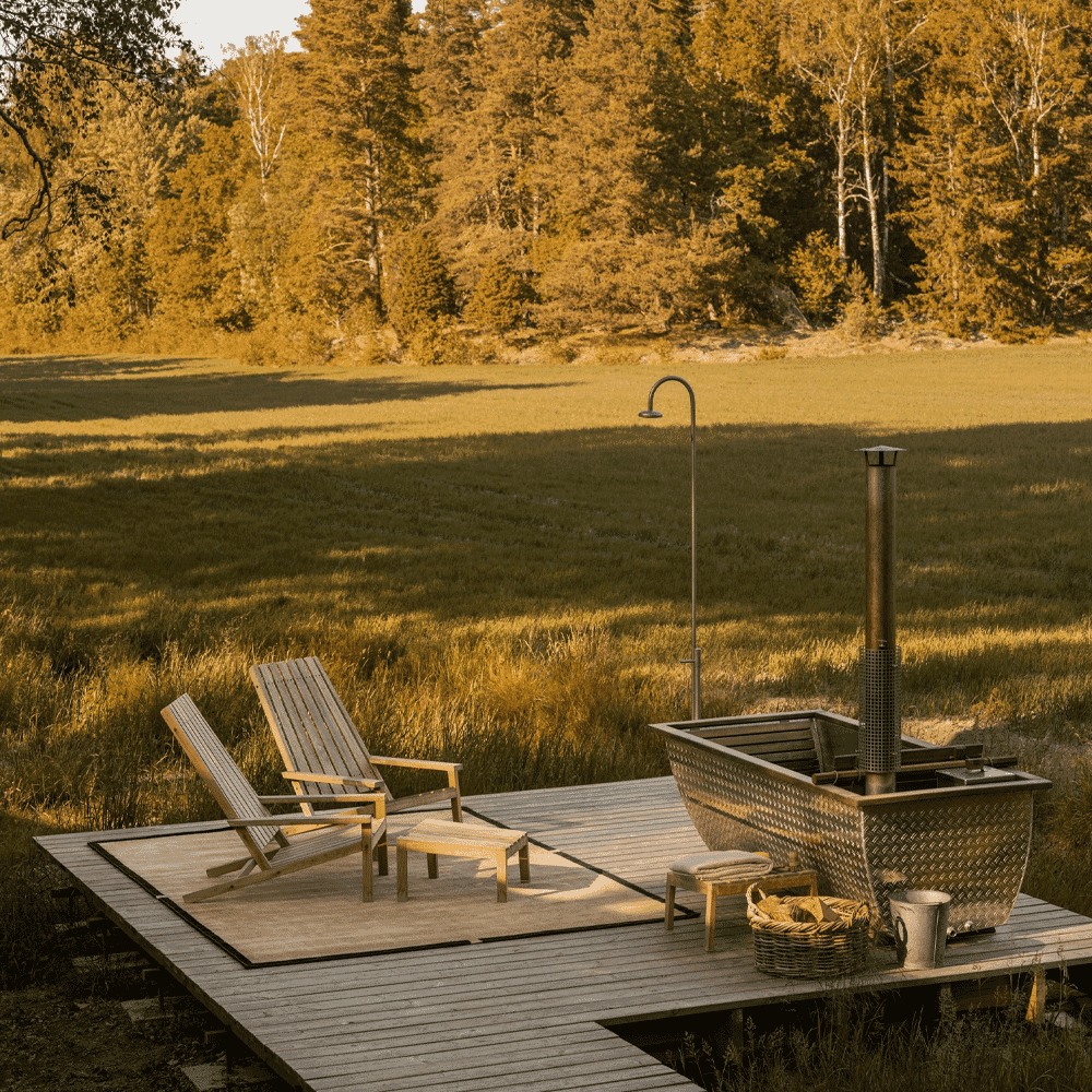 Wooden lounge chairs and a metal hot tub on a deck overlooking a golden autumn field.