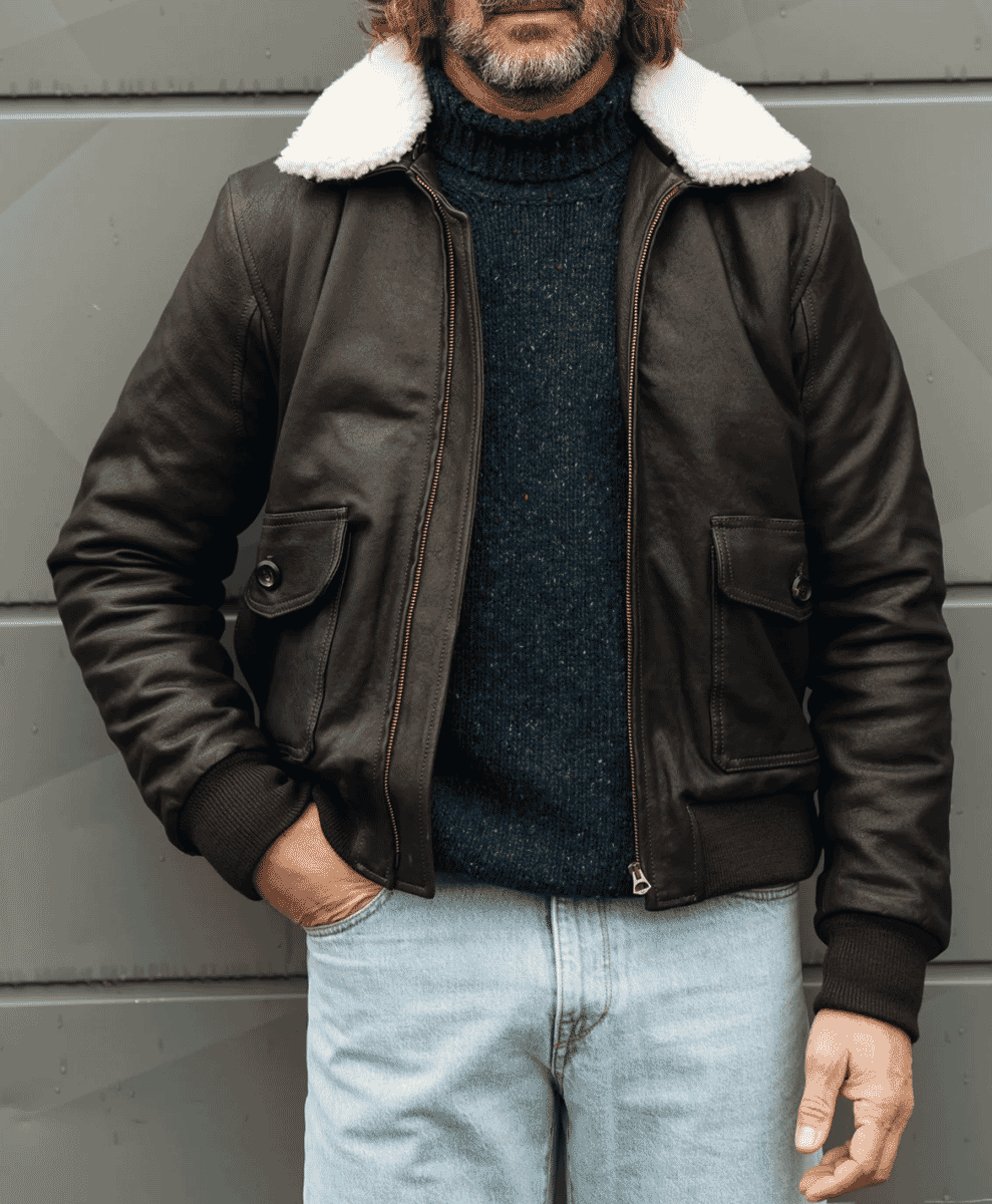 A man wearing a dark brown shearling-lined bomber jacket over a navy turtleneck sweater.