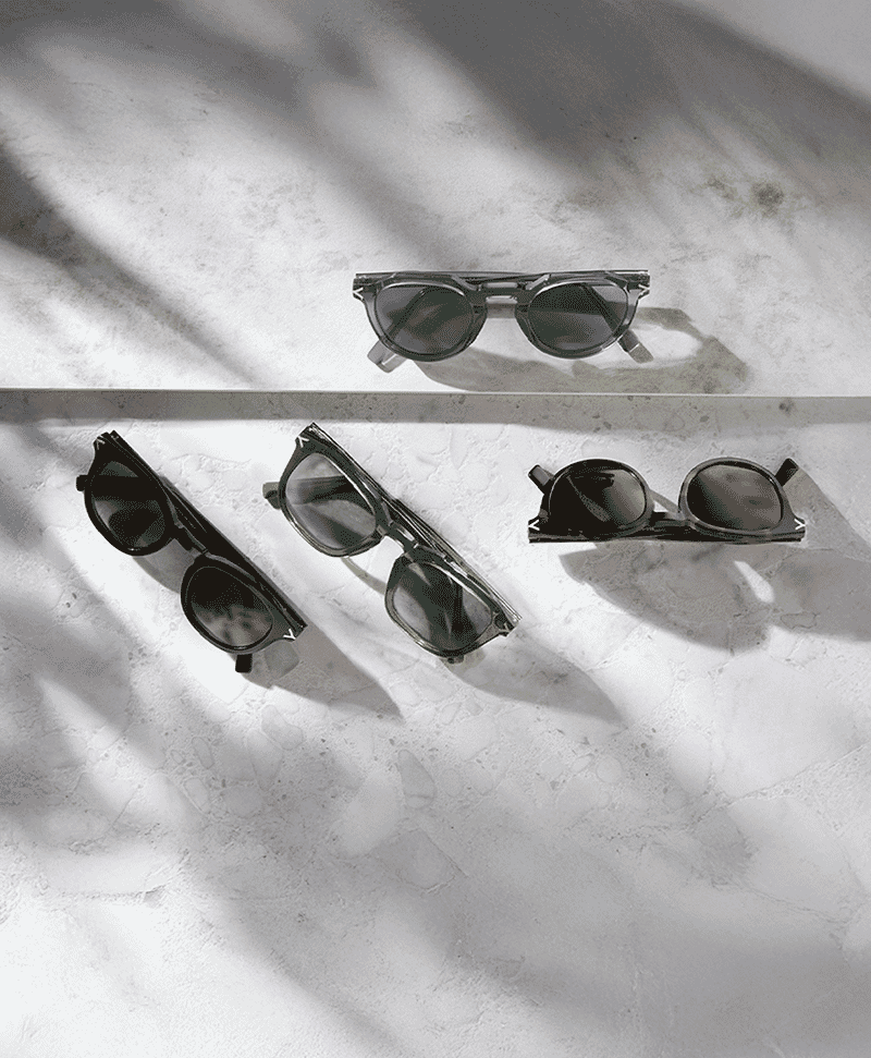 Five pairs of various sunglasses arranged on a textured white surface with shadows.