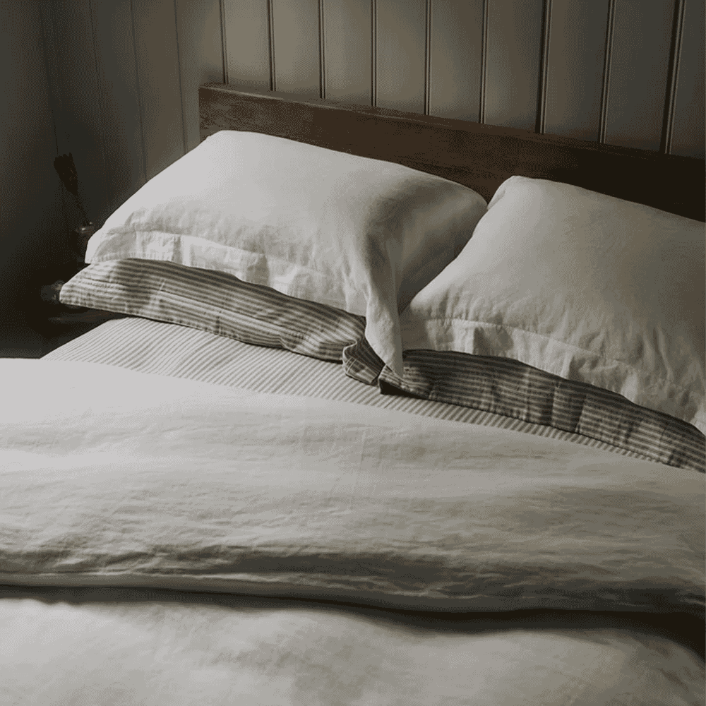 Rustic bedroom scene with a bed featuring white linen sheets and striped pillows.