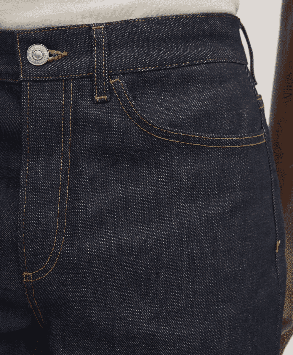 Close-up of dark indigo denim jeans featuring contrasting tan stitching.