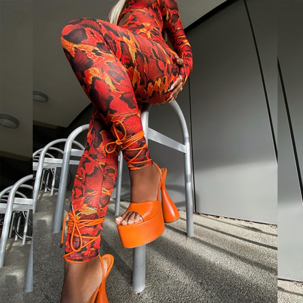 A model wearing a flame-print bodysuit and vibrant orange platform heels posing on a metal stool.