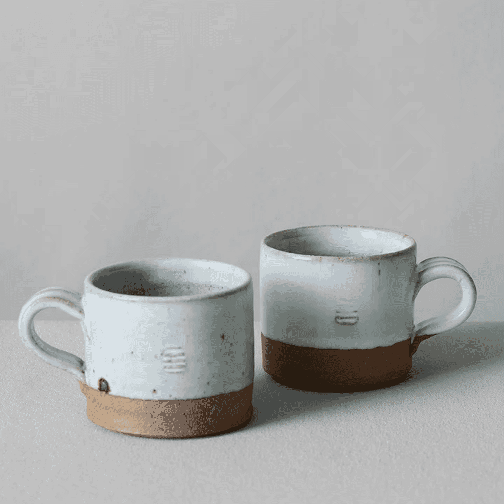 Two handmade ceramic mugs with white glaze and exposed brown clay bases.
