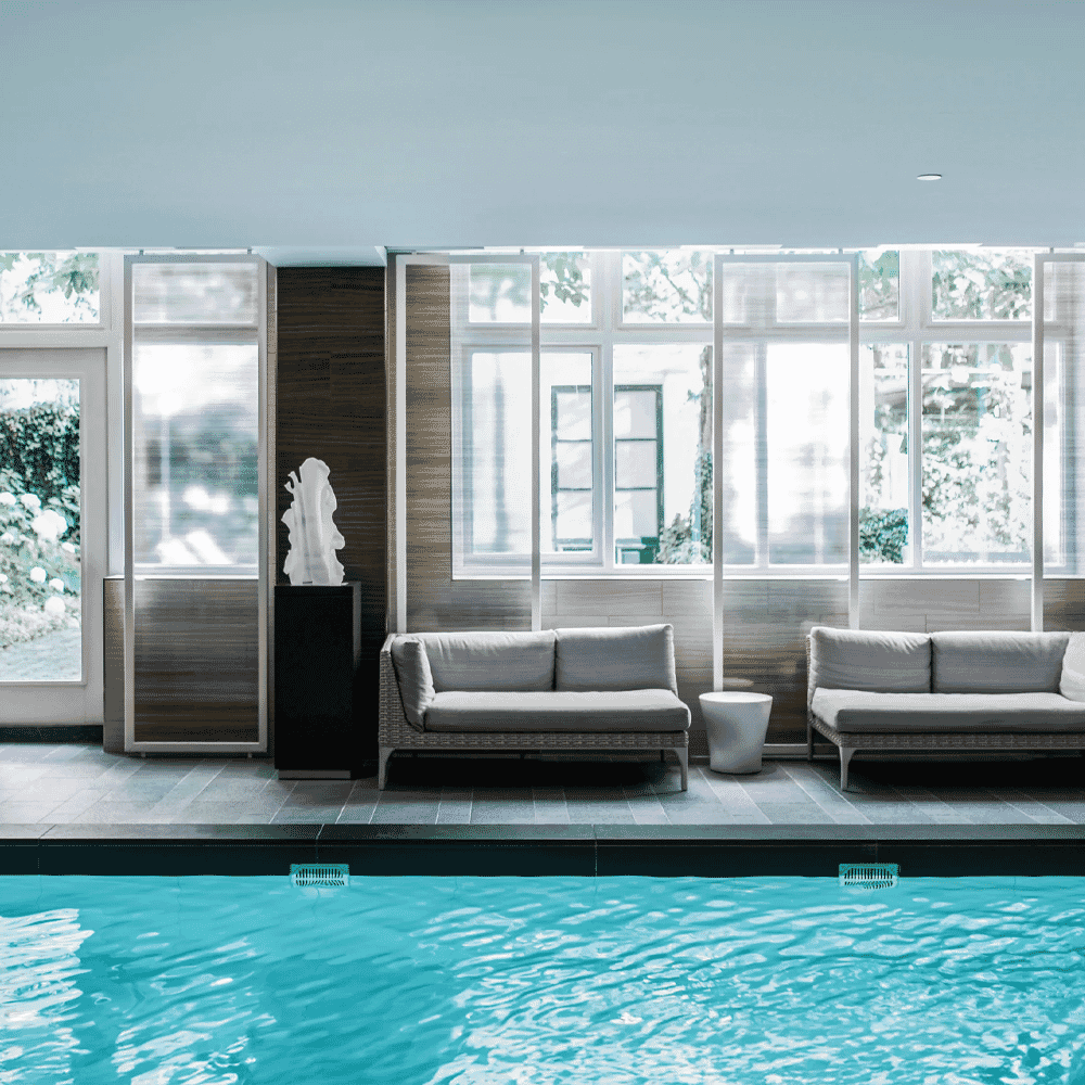Luxury indoor pool area with modern furniture and serene blue water.