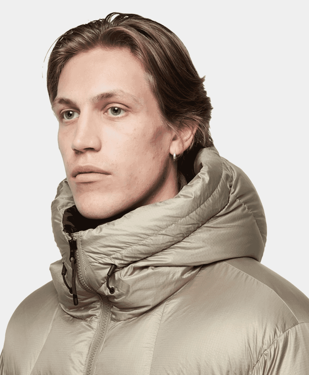 A man wearing a light beige Goldwin puffer jacket with a high padded collar.