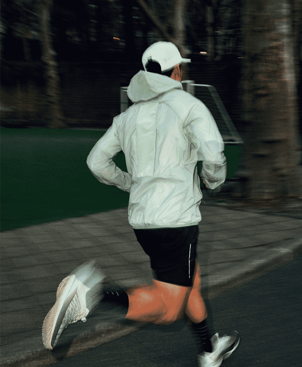 A runner in a white hooded technical jacket captured in motion at dusk.