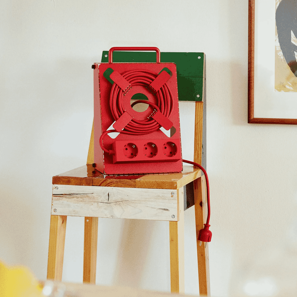A bright red industrial-style power strip with a coiled cord placed on a rustic wooden chair.