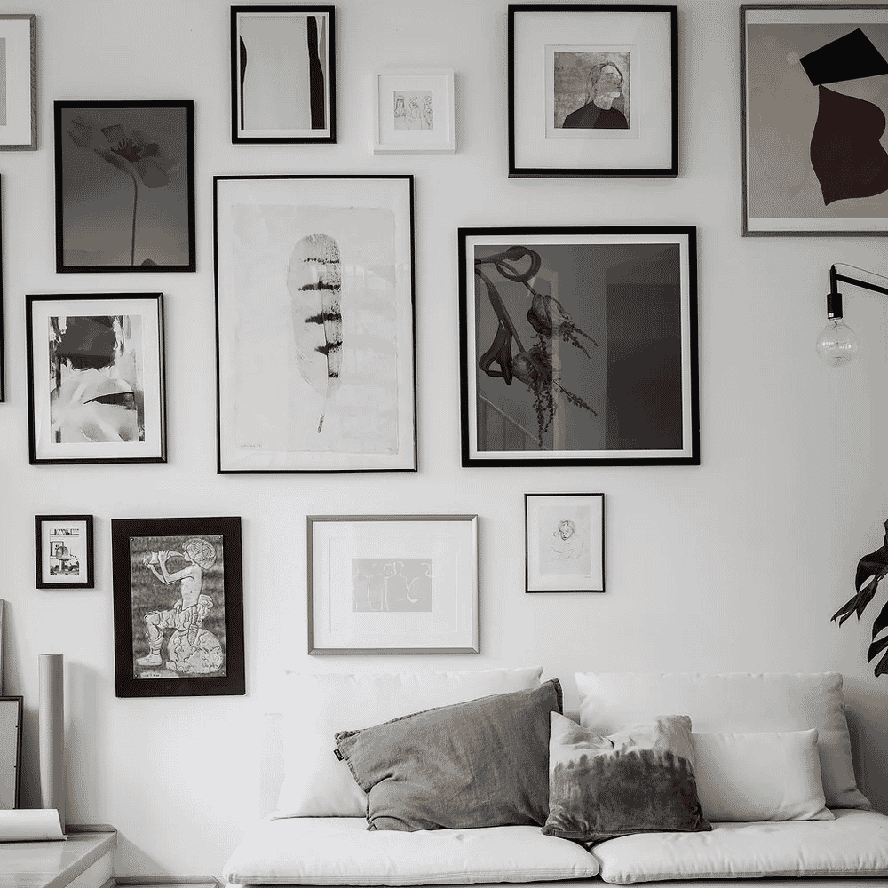 A monochrome living room gallery wall with various black and white art pieces above a white sofa.