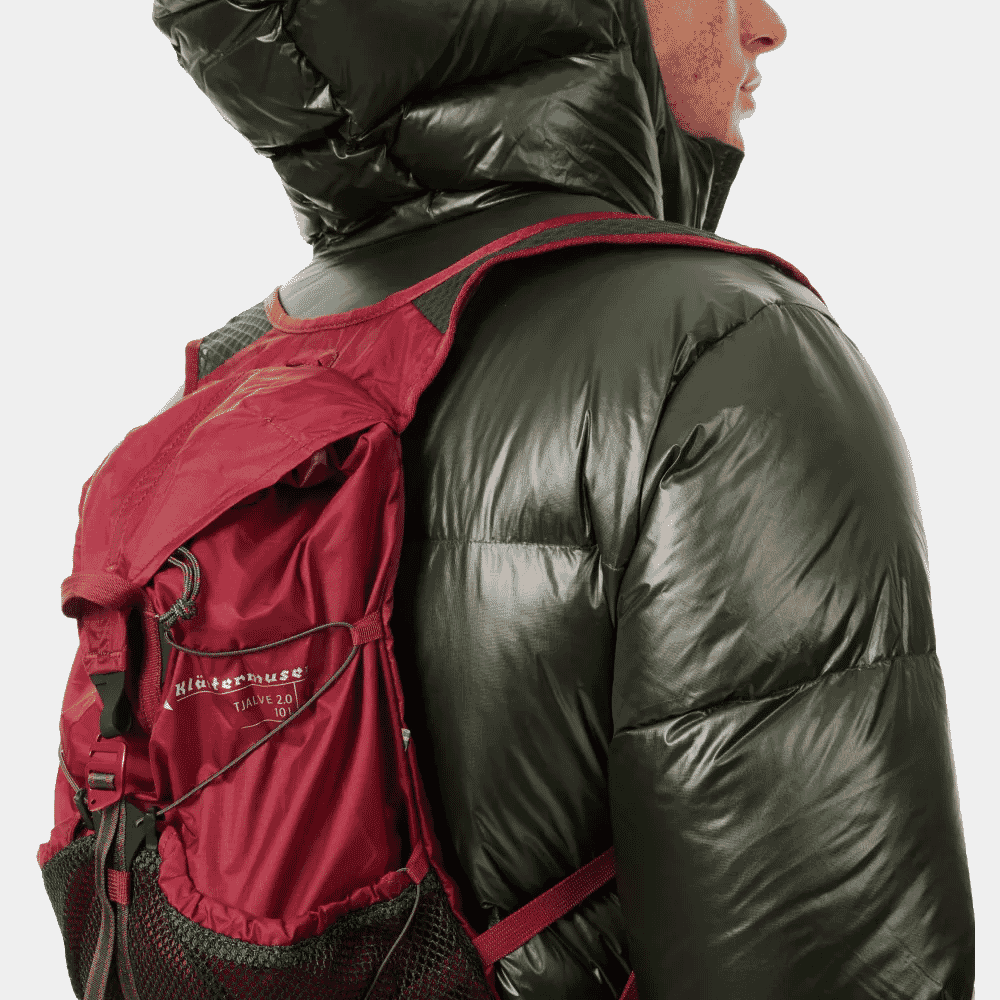 A man in a black puffer jacket wearing a red Klättermusen Tjälve 2.0 backpack.