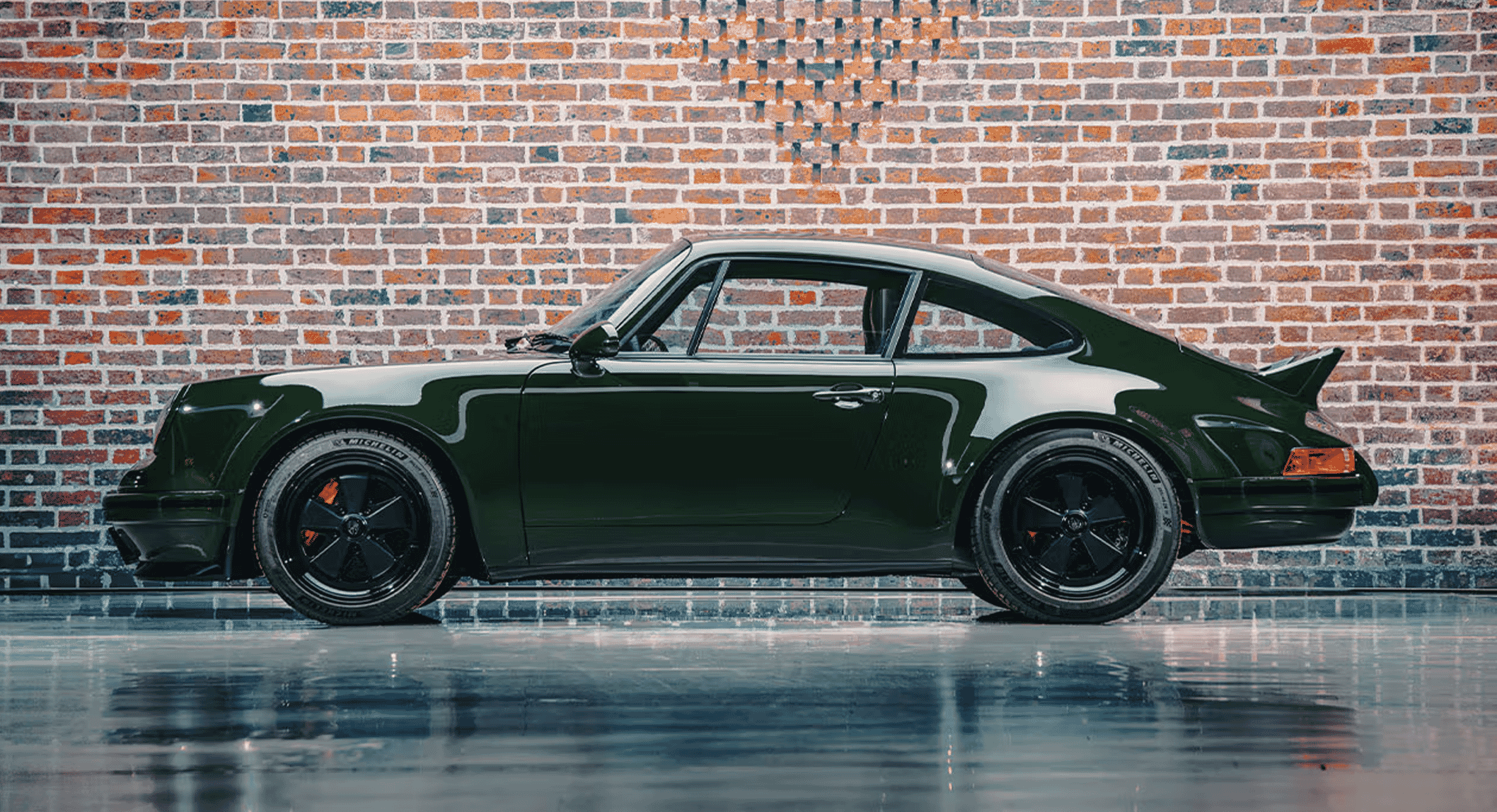 Sleek dark green Porsche 911 with black wheels in an industrial garage setting.