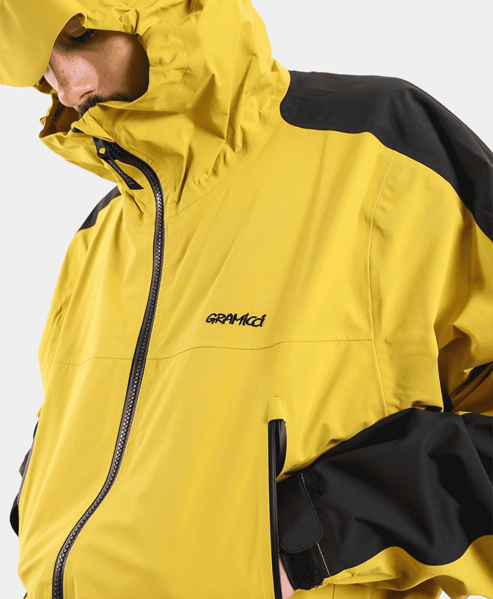Close-up of a model wearing the yellow and black Gramicci hooded jacket showing the brand logo.