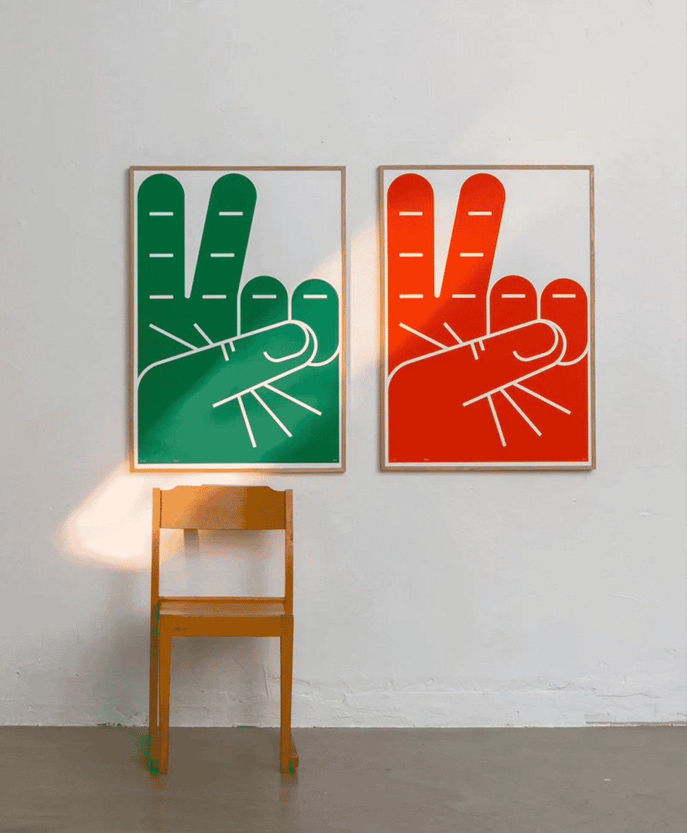 Two framed peace sign posters hanging on a white wall above a wooden chair.