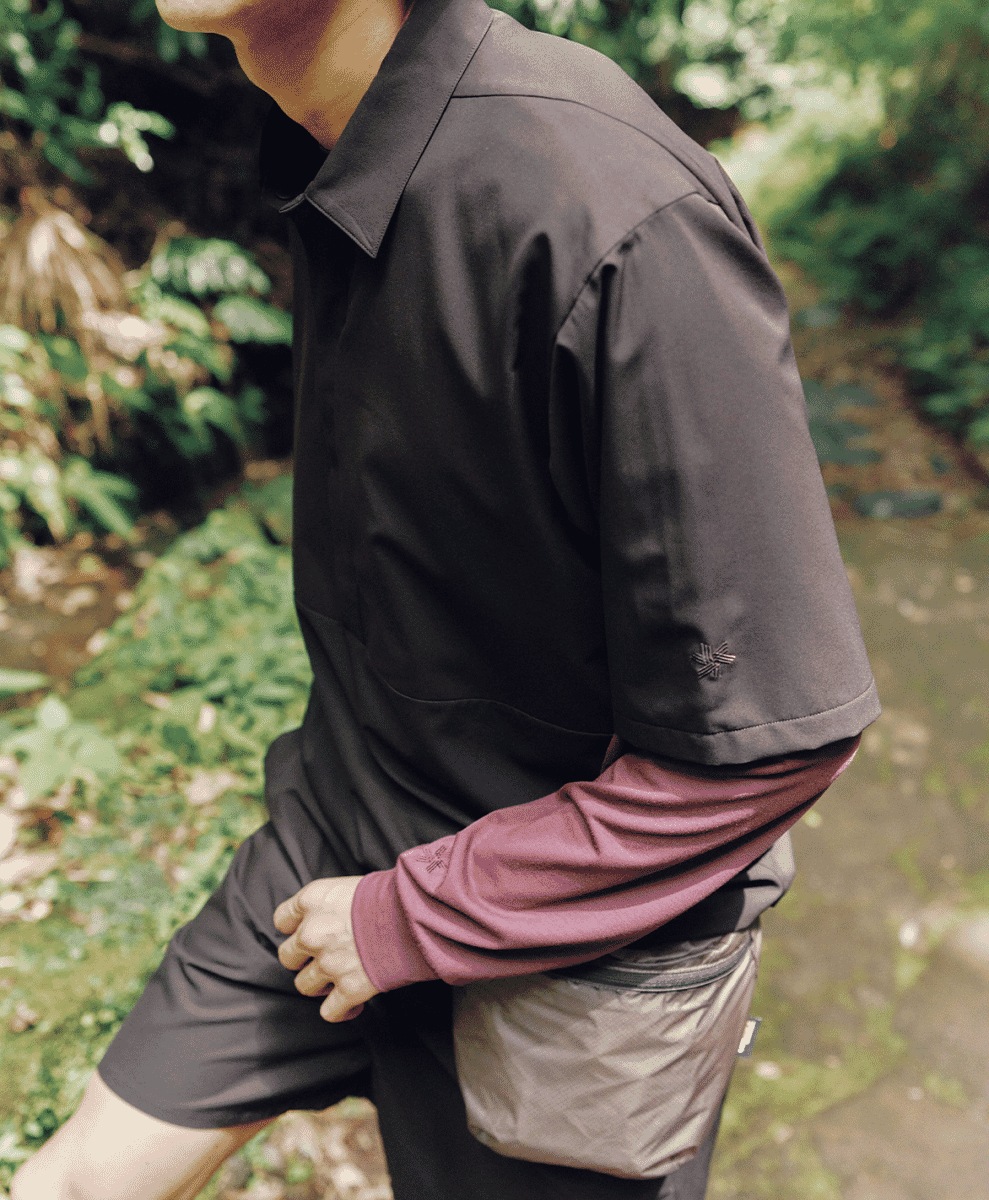 Man walking on a forest path wearing a black short-sleeve shirt layered over a burgundy long-sleeve top.