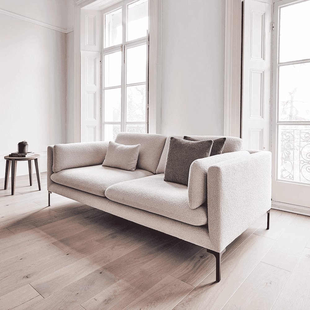 Light-colored bouclé sofa with dark legs and throw pillows in a minimalist room.