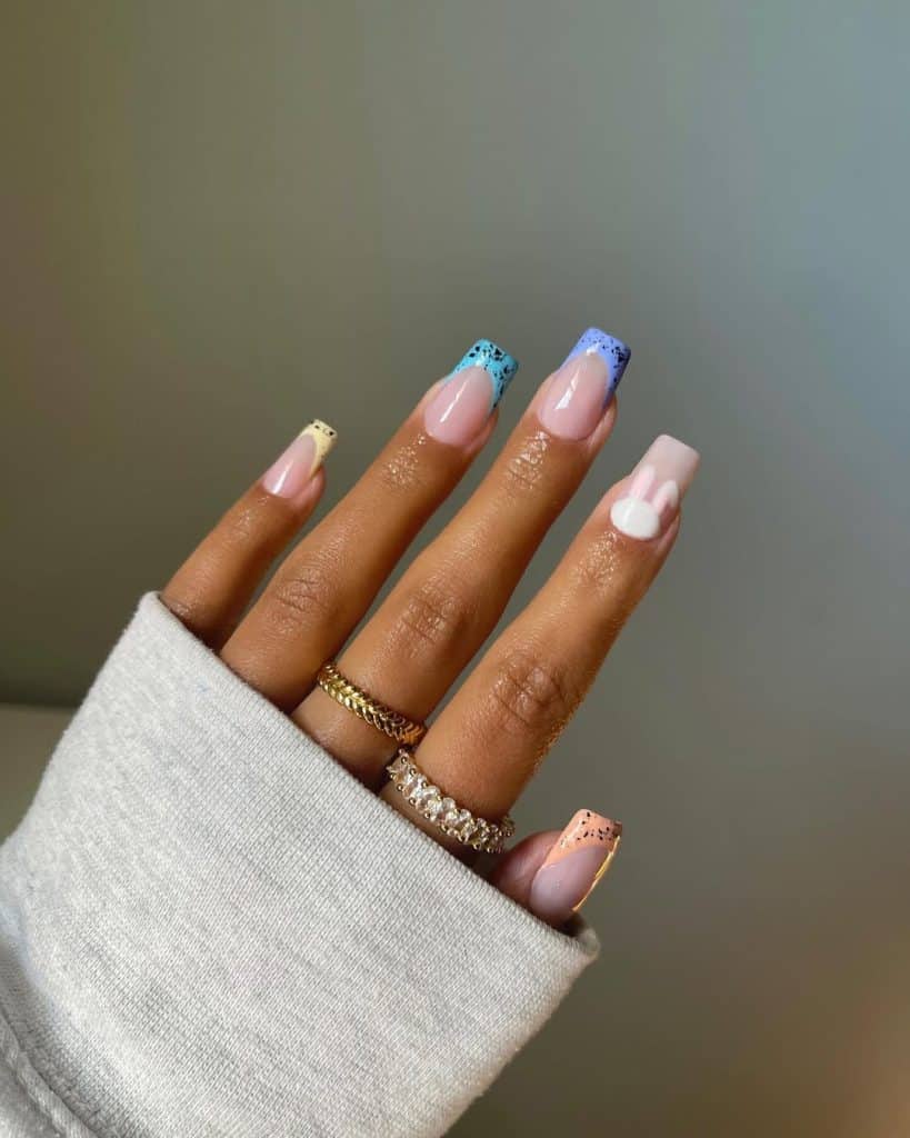 Hand with colorful speckled nails wearing a light gray ribbed sweater.